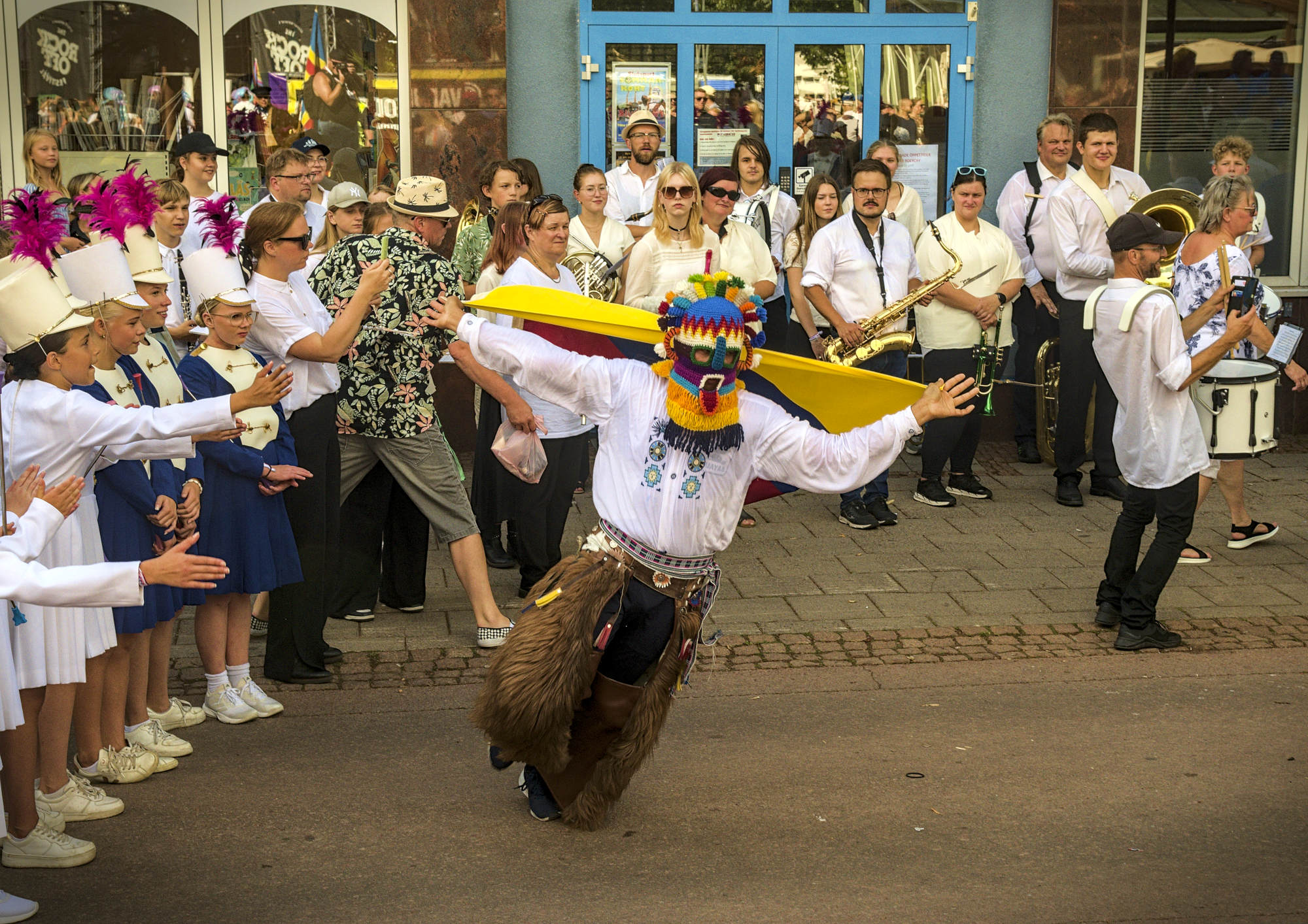 I mitten dansar skeppet Guayas maskot på en väg i staden. Runtom står barn i paraduniform och musiker. Längs med en husvägg syns även övrig publik.