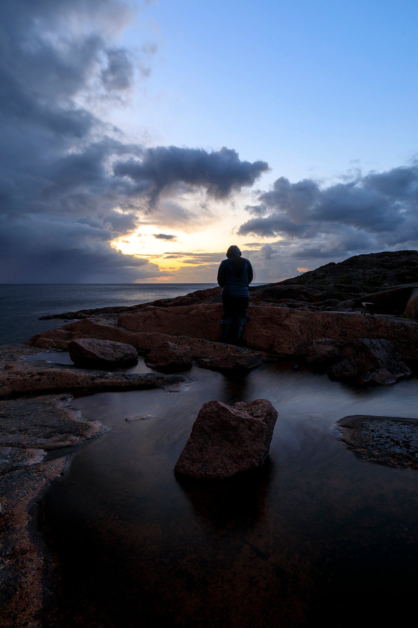 Person på en klippig strand och mörka moln i bakgrunden
