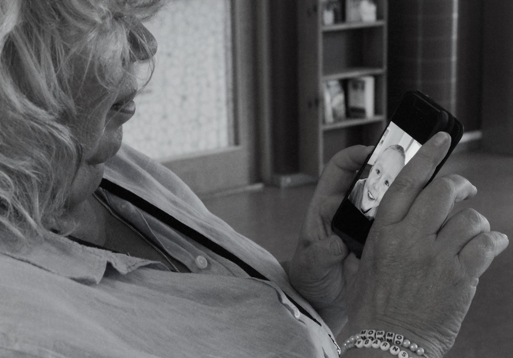 Mormor som pratar med barnbarn över mobilen. Svartvit bild.