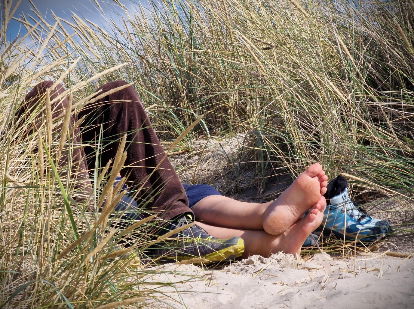 Ett par som ligger på stranden. Bara ben o fötter syns.