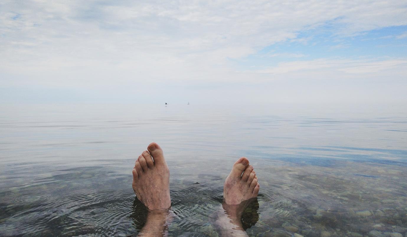 Fötter i vatten, utsikt mot havet.